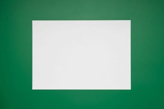 Empty white paper sheet isolated on green background.