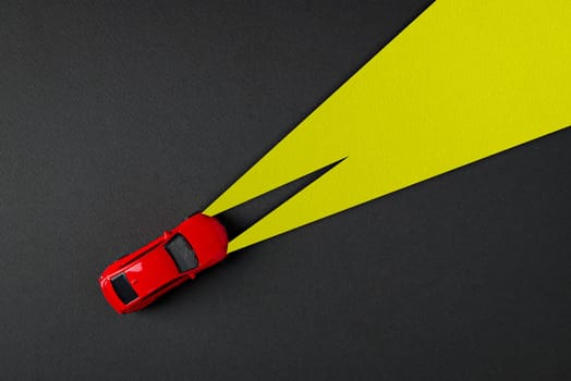 Top view of red toy car and yellow headlights on dark gray background