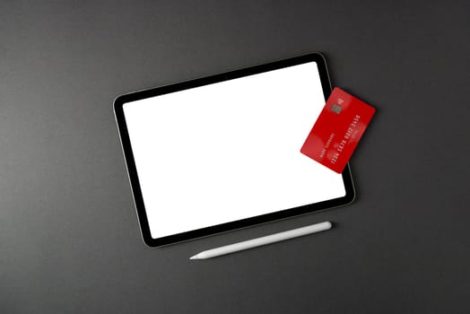 Credit card lying on tablet with blank screen on dark gray table