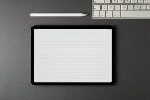 Tablet with lined notepaper on the screen and a keyboard and stylus pen on a dark gray table