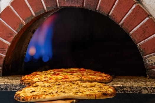 Mixed pizza fresh from the pizza oven with flames visible in the background