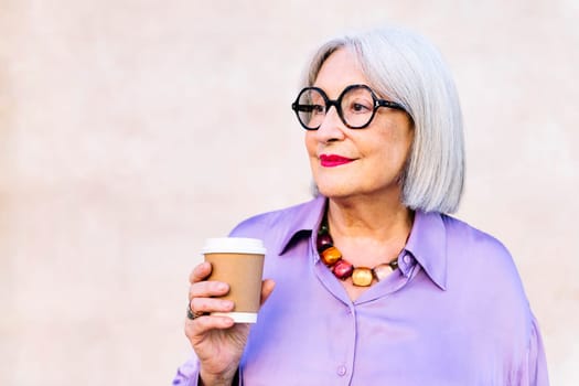 smiling senior woman holding a takeaway coffee in her hand, concept of elderly people leisure and active lifestyle, copy space for text