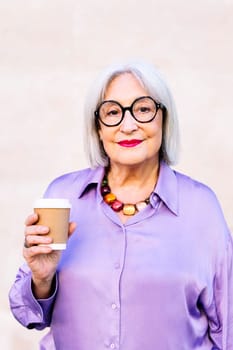 smiling senior woman looking at camera holding a takeaway coffee in her hand, concept of elderly people leisure and active lifestyle