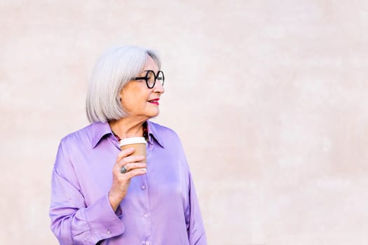 profile portrait of a smiling senior woman holding a takeaway coffee in her hand, concept of elderly people leisure and active lifestyle, copy space for text