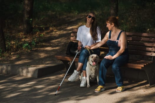 Blind caucasian woman sitting on bench with guide dog and pregnant friend