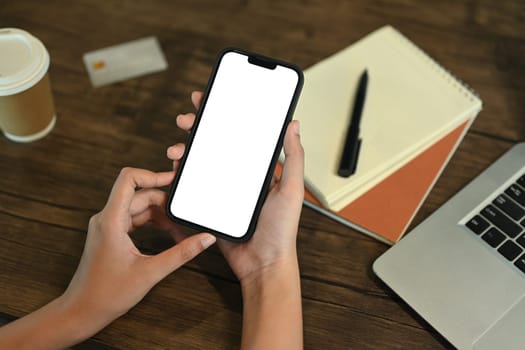 Unrecognizable young woman sitting at desk with laptop and using mobile phone.