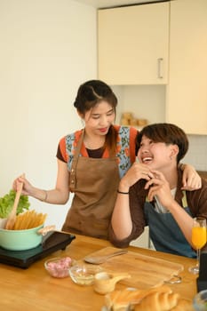 Cheerful young couple having fun cooking in the kitchen at home on weekend.