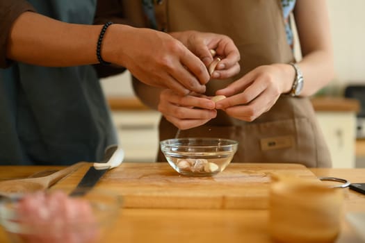 Hands of young couple peeling garlic on wooden chopping board. Healthy lifestyle concept.