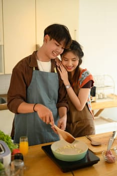 Portrait of affectionate young couple wearing aprons cooking together in the kitchen at home.