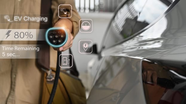 Businessman holding an electric vehicle charging gun connector standing in home garage.