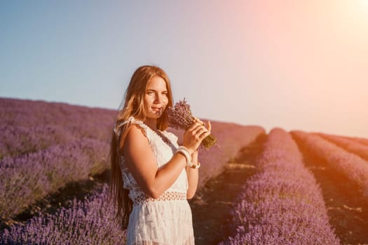 Close up portrait of young beautiful woman in a white dress and a hat is walking in the lavender field and smelling lavender bouquet.