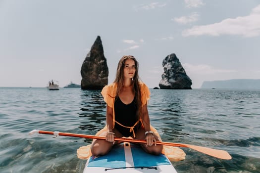 Close up shot of beautiful young caucasian woman with black hair and freckles looking at camera and smiling. Cute woman portrait in a pink bikini posing on a volcanic rock high above the sea