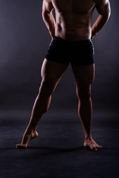 Muscular male legs, man in a studio, dark background