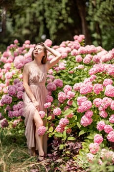 Hydrangeas Happy woman in pink dress amid hydrangeas. Large pink hydrangea caps surround woman. Sunny outdoor setting. Showcasing happy woman amid hydrangea bloom