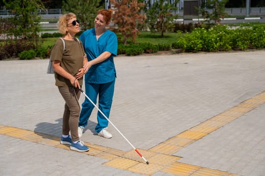 A nurse accompanies an elderly blind woman on a walk