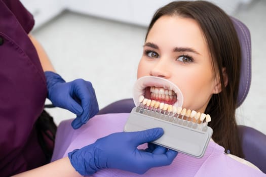 Woman patient and shades of the implants for teeth whitening in doctors hands.