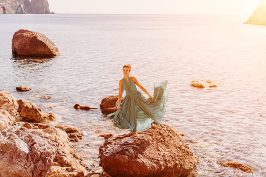 Woman green dress sea. Woman in a long mint dress posing on a beach with rocks on sunny day. Girl on the nature on blue sky background