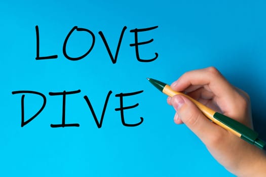 Children hand with pen write on a blue white background. Writing hand. Word Love Dive