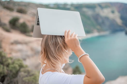 Freelance women sea working on the computer. Good looking middle aged woman typing on a laptop keyboard outdoors with a beautiful sea view. The concept of remote work