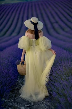 Back view woman lavender sunset. Happy woman in yellow dress holds lavender bouquet. Aromatherapy concept, lavender oil, photo session in lavender.