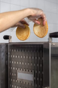 Conveyor toaster for frying burger buns to a crisp. The cook puts the halves of the bun into the device.
