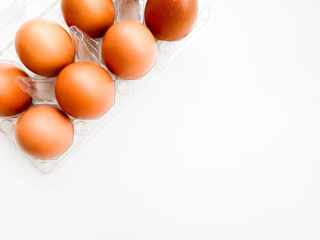 Brown eggs in transparent plastic carton on white background, top corner view. Concept of organic produce, breakfast essentials, and healthy eating with copy space. High quality photo