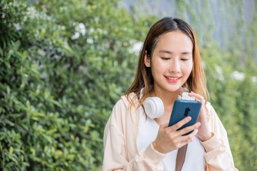 In an urban garden a cheerful young woman uses wireless headphones to immerse herself in the joy of selecting and listening to her favorite music. Her carefree dance underlines beauty of the season.