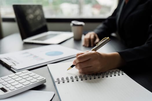 Business woman working in office writing plan on note book and use computer laptop to plan marketing strategy.