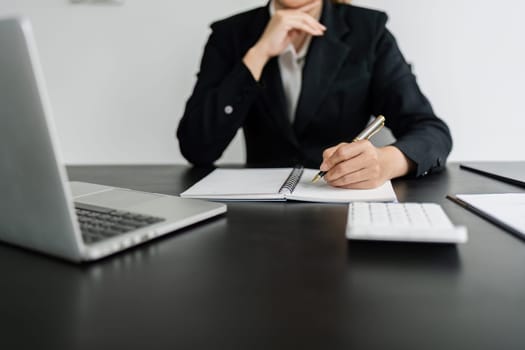 Business woman working in office writing plan on note book and use computer laptop to plan marketing strategy.