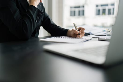 Business woman working in office writing plan on note book and use computer laptop to plan marketing strategy.