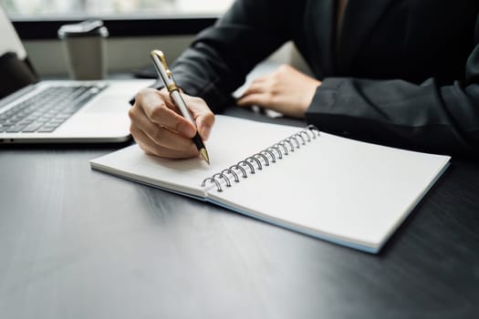 Business woman working in office writing plan on note book and use computer laptop meeting online.