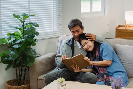 Retired elderly couple sits on couch in their home reading relaxing book. Senior Activity Concept.