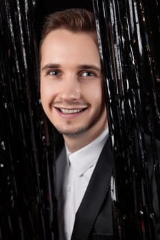 Happy handsome man in black jacket smiling on glitter background.