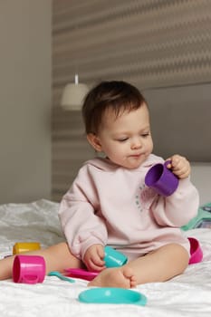 happy cute little child girl playing and pretending drinking tea from toy cups on bed