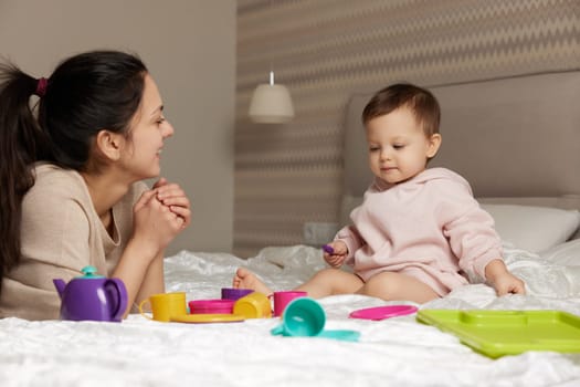 smiling mother and little child daughter playing tea party and spending time together in bedroom, family having fun