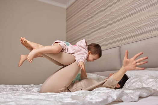 Happy Caucasian mother lifting in air cute little child daughter in bedroom