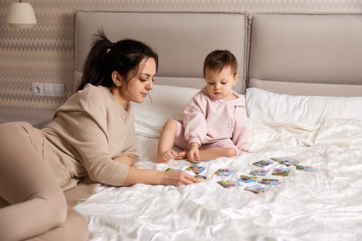pretty mother playing puzzle together with her little child girl in bedroom