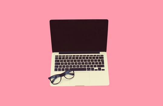 Close up laptop with blank black screen and eyeglasses on pink background