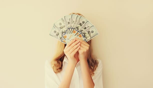 Portrait of happy woman holding cash money in dollar bills in her hands covering her face
