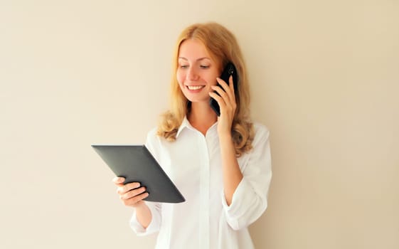 Portrait of caucasian young woman employee with digital tablet computer or folder with documents and calling on mobile phone in office