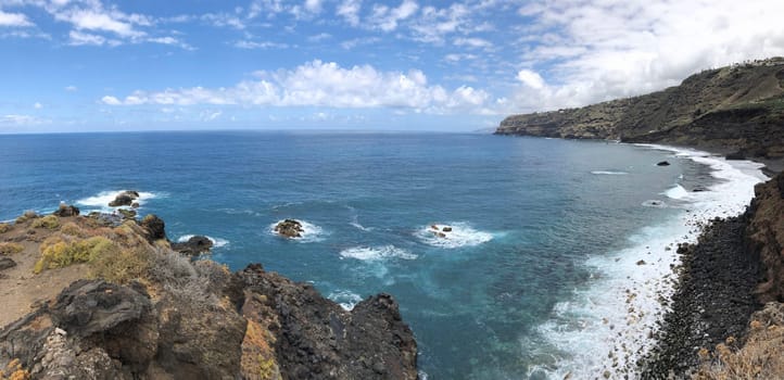 Panoramic coastal landscape rocky cliff, sea waves and blue sky with clouds