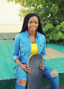 Portrait of happy smiling young african woman model posing with skateboard in the city