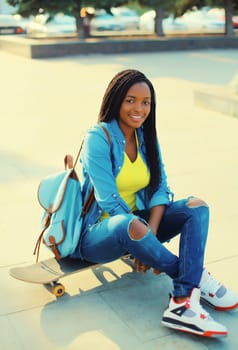 Portrait of happy smiling young african woman model posing with skateboard in the city