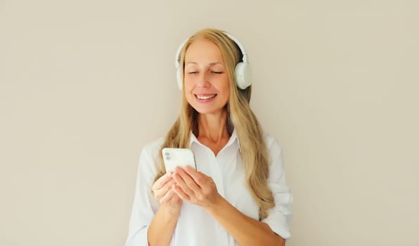 Happy smiling middle aged woman listening to music with mobile phone in headphones on studio background