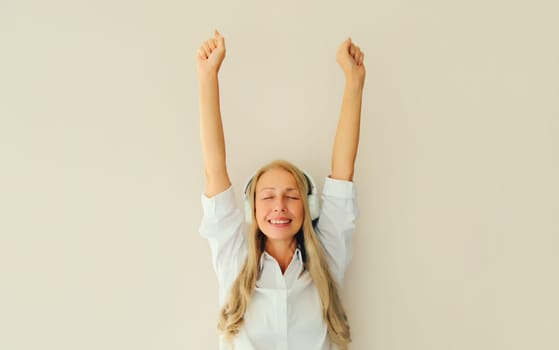 Happy cheerful middle aged woman listening to music dancing having fun in headphones on white background