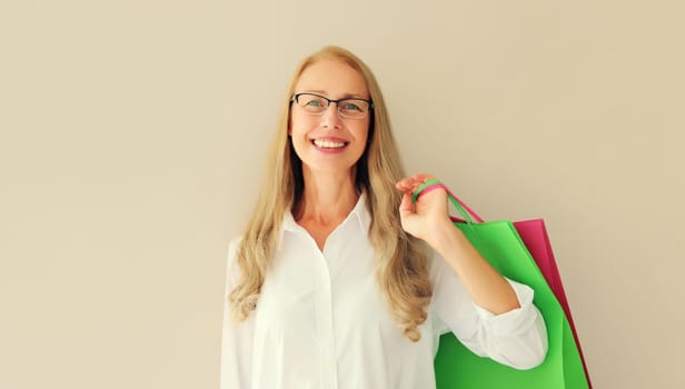 Portrait of beautiful happy smiling middle aged woman posing with colorful shopping bags in eyeglasses on studio background