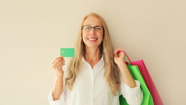 Portrait of happy smiling caucasian middle aged woman holding plastic credit bank card with shopping bags on studio background