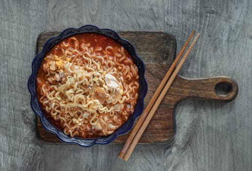Spicy tom yum Instant noodles topped with egg and sliced ​​shallots in ceramic bowl and chopstick on a wooden cutting board. Easy noodle food, Top view, Space for text, Selective focus.