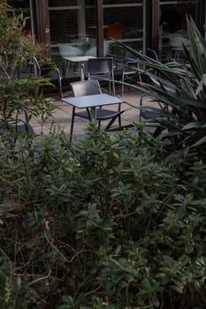 Empty tables and chairs shadows outside a cafe with looking through a gap the bushes. Sunlight shine through tables and chairs in the afternoon, Space for text, Selective focus.