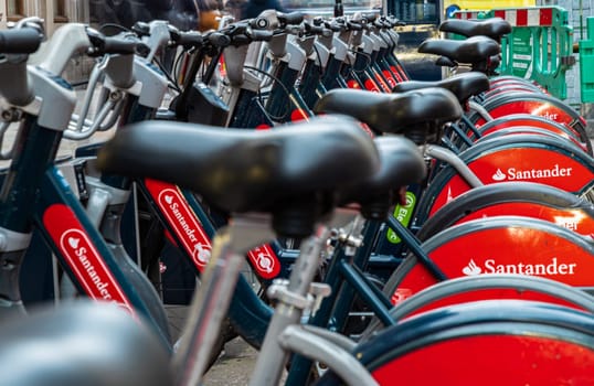 London, UK - Feb 15, 2024 - Public rental bicycle for transportation bike to work and travel in center city of London, View of Bicycle seat and Bicycle handlebars, Row of Urban electric red bikes charging batteries, Urban transport, Shared rental bike, Space for text, Selective focus.